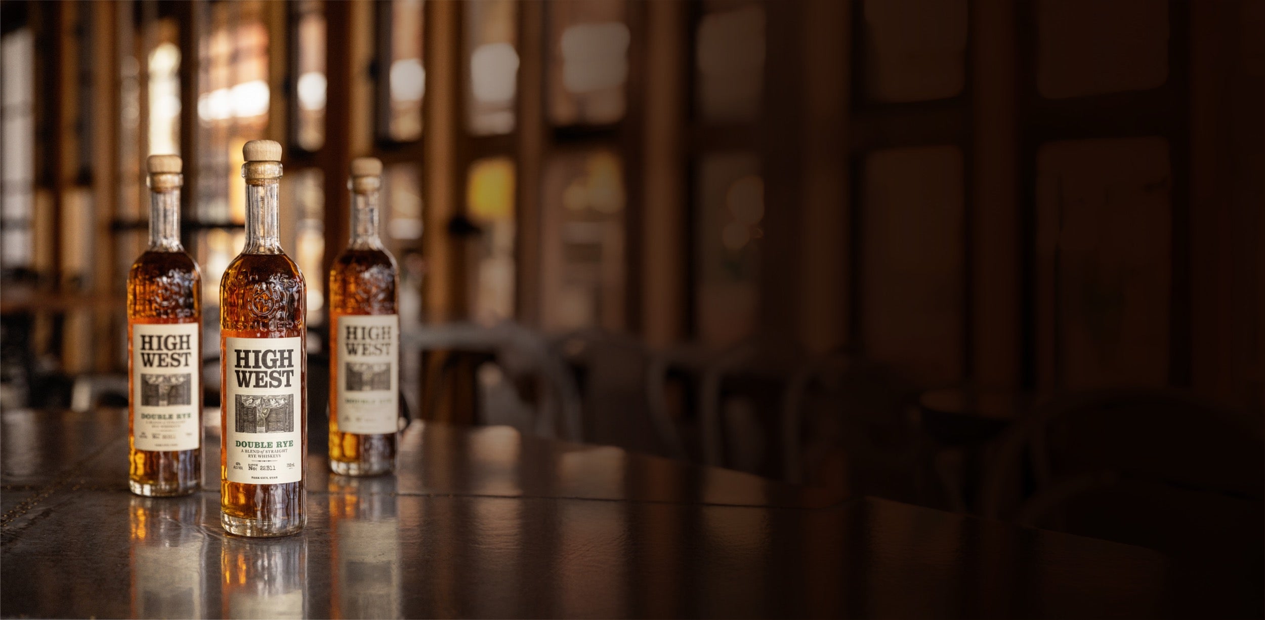 Three bottles of High West whiskey on a wooden table with blurred background